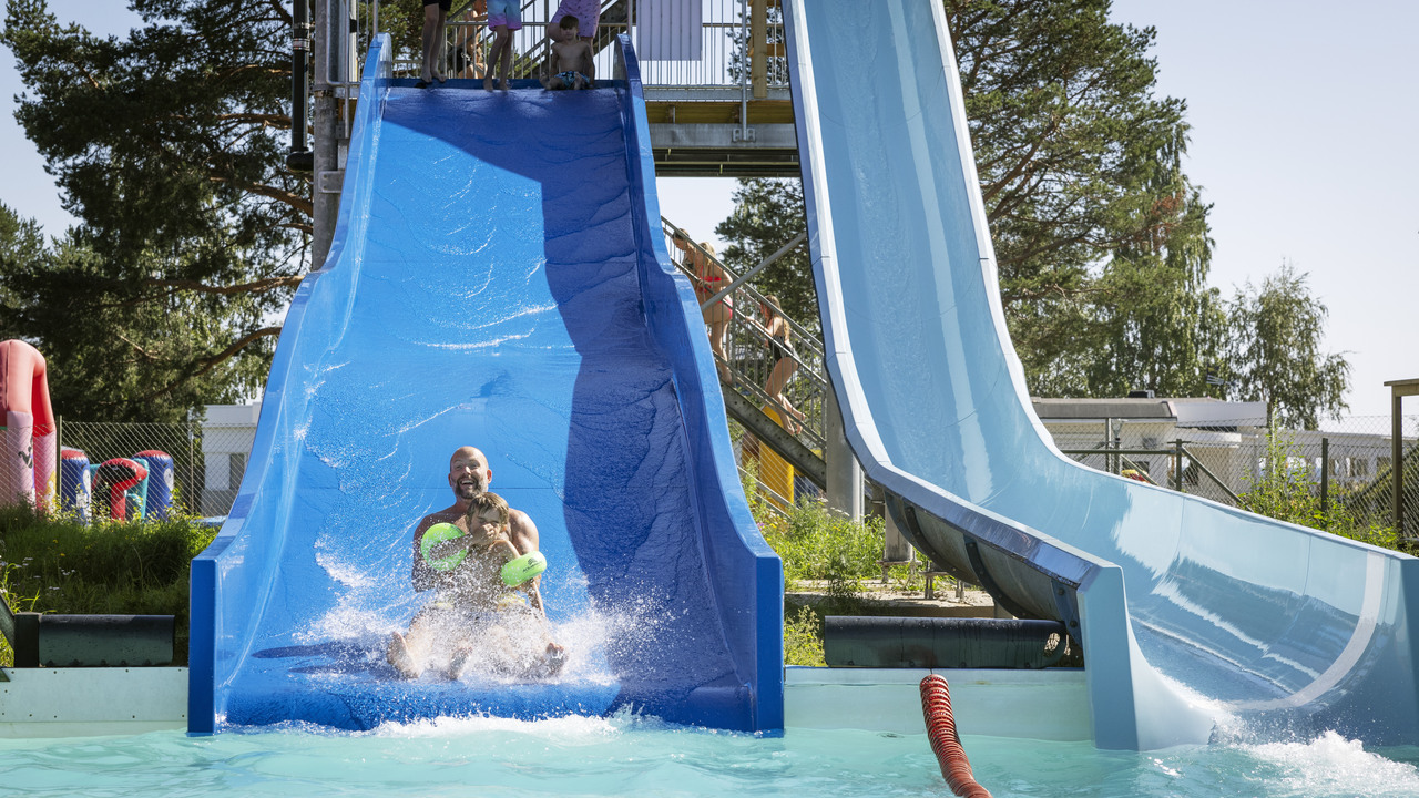 En man åker med ett barn i vattenruschkanan ner i poolen.