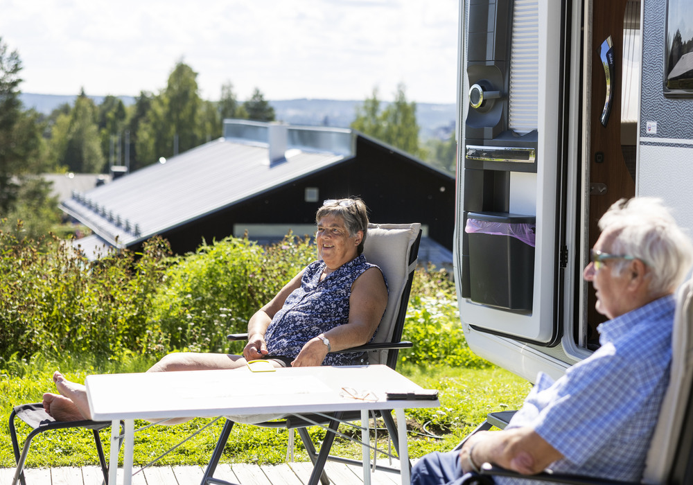 Ett äldre par sitter i varsin solstol utanför sin husbil och njuter av solen och sällskapet.