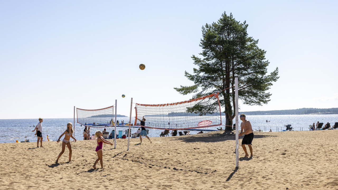 En familj spelar volleyboll på stranden.