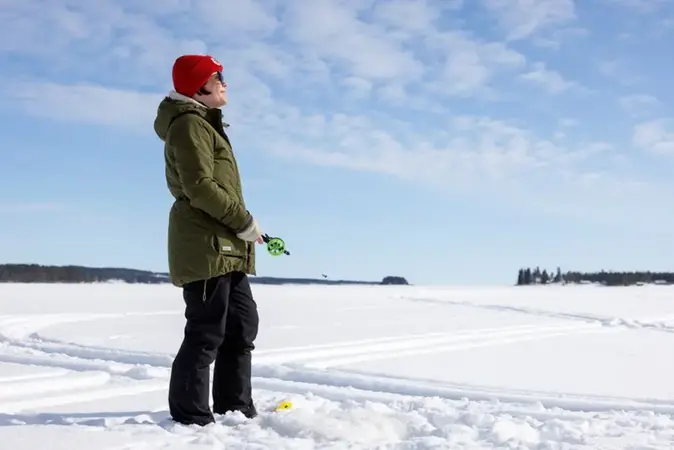 Kvinna står på isen och pimplar fisk