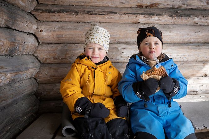 Två barn som äter grillad macka i ett vindskydd