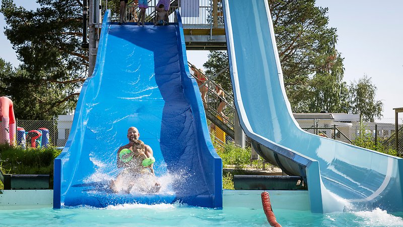En man åker med ett barn i vattenruschkanan ner i poolen.