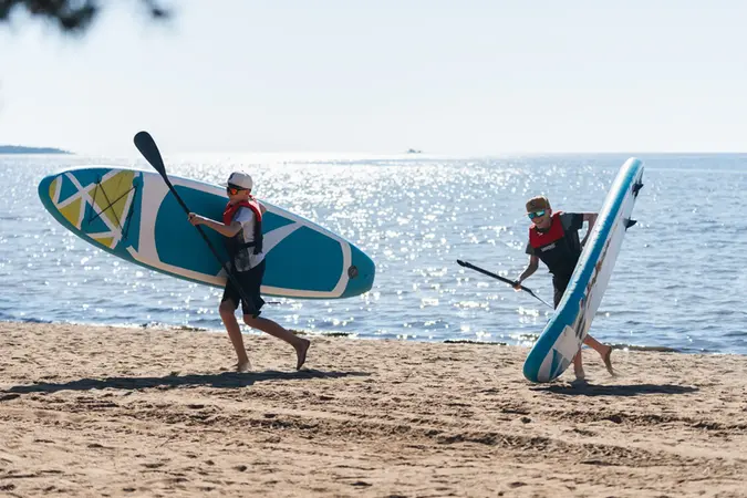 Två personer på stranden med var sin sup-bräda