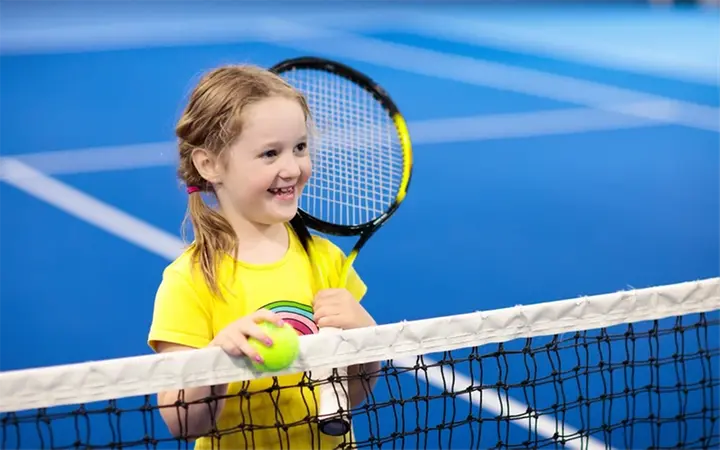 Tjej som står med tennisracket bredvid ett tennisnät