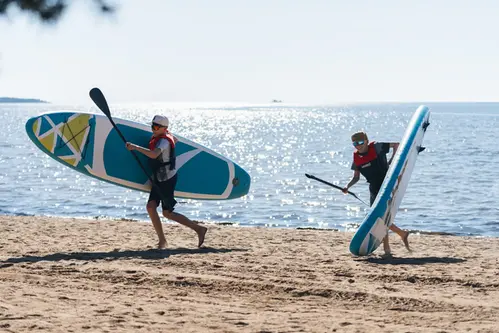 Två personer som står på stranden med var sin stand up board